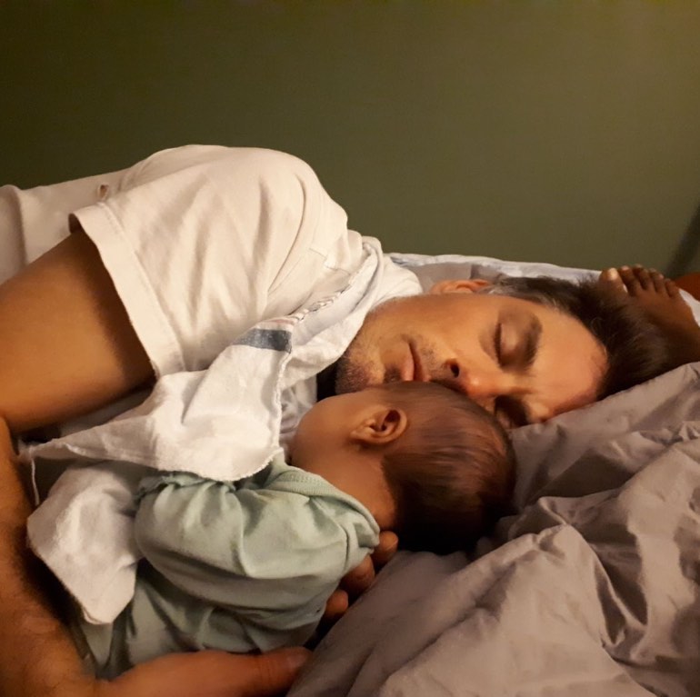 Casey doses in bed with his arms around baby Zahra.