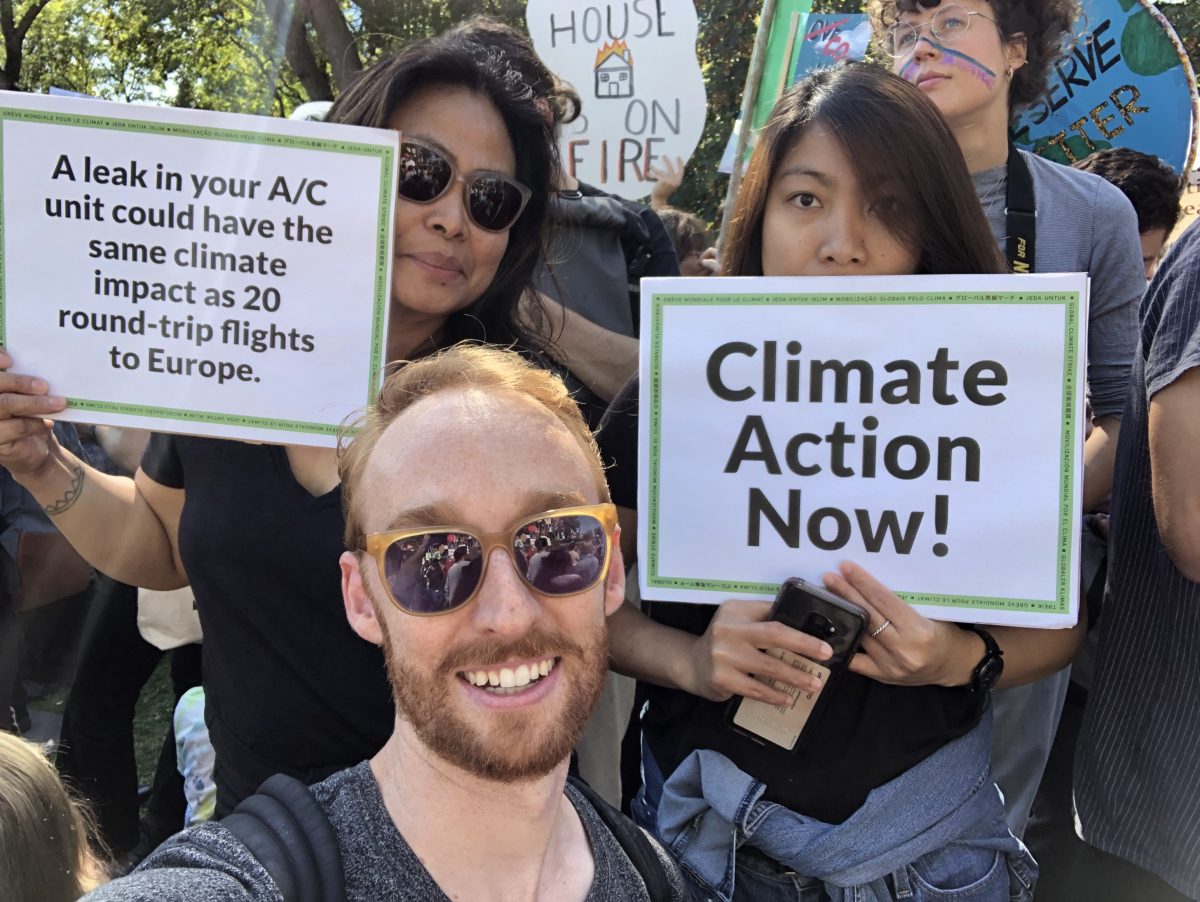 Norlinda holds a sign that reads 'A leak in your A/C unit could have the same climate impact as 20 round-trip flights to Europe." April's sign reads "Climate Action Now!"
