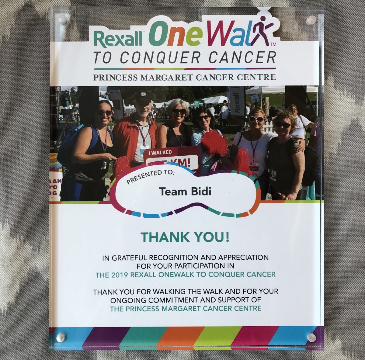A plaque with title, "Rexall One Walk to Conquer Cancer. Princess Margaret Cancer Centre." A photo of Team Bidi and the text "Presented to Team Bidi. Thank you! In grateful recognition and appreciation for your participation in the 2019 REXALL ONEWALK TO CONQUER CANCER. Thank you for walking the walk and for your ongoing commitment and support of THE PRINCESS MARGARET CANCER CENTRE"